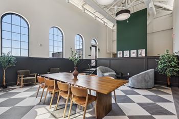 A long wooden table is surrounded by chairs in a room with a checkered floor.